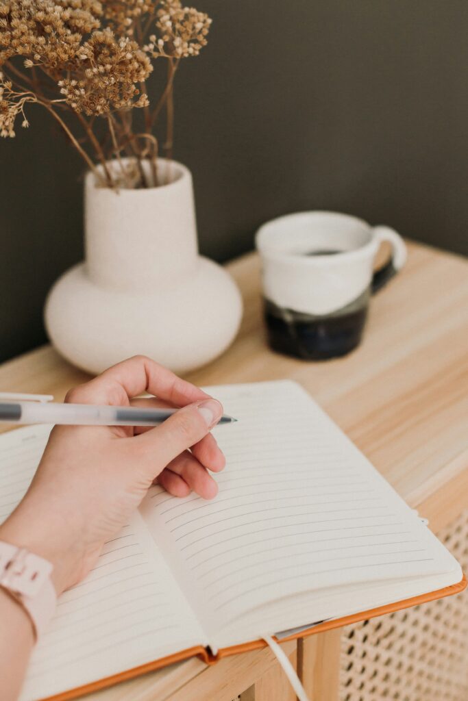 A writer's hand journaling next to coffee and dried flowers, mid-revision session